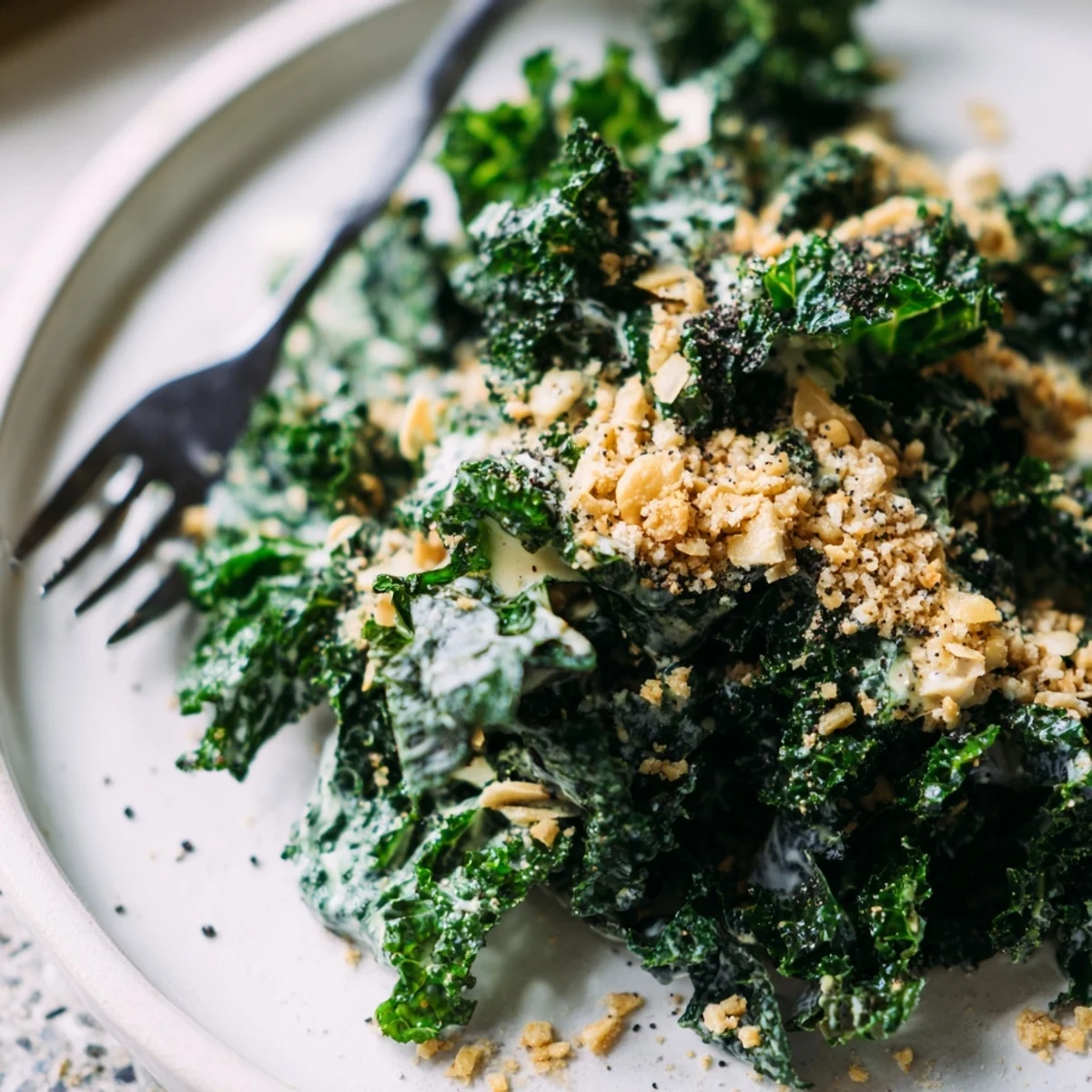 A close-up of vibrant massaged kale tossed in creamy garlic Parmesan dressing, topped with golden toasted breadcrumbs and shaved Parmesan for a savory side dish.