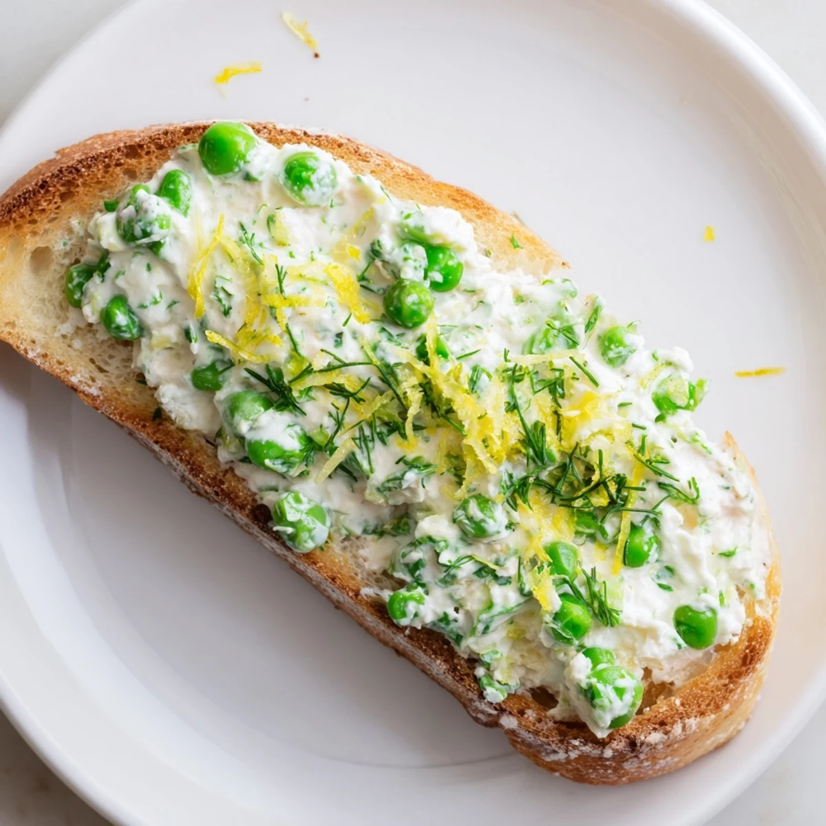 Creamy Pea & Mint Ricotta Toast on golden sourdough, topped with fresh lemon zest and bright peas for a vibrant spring breakfast.