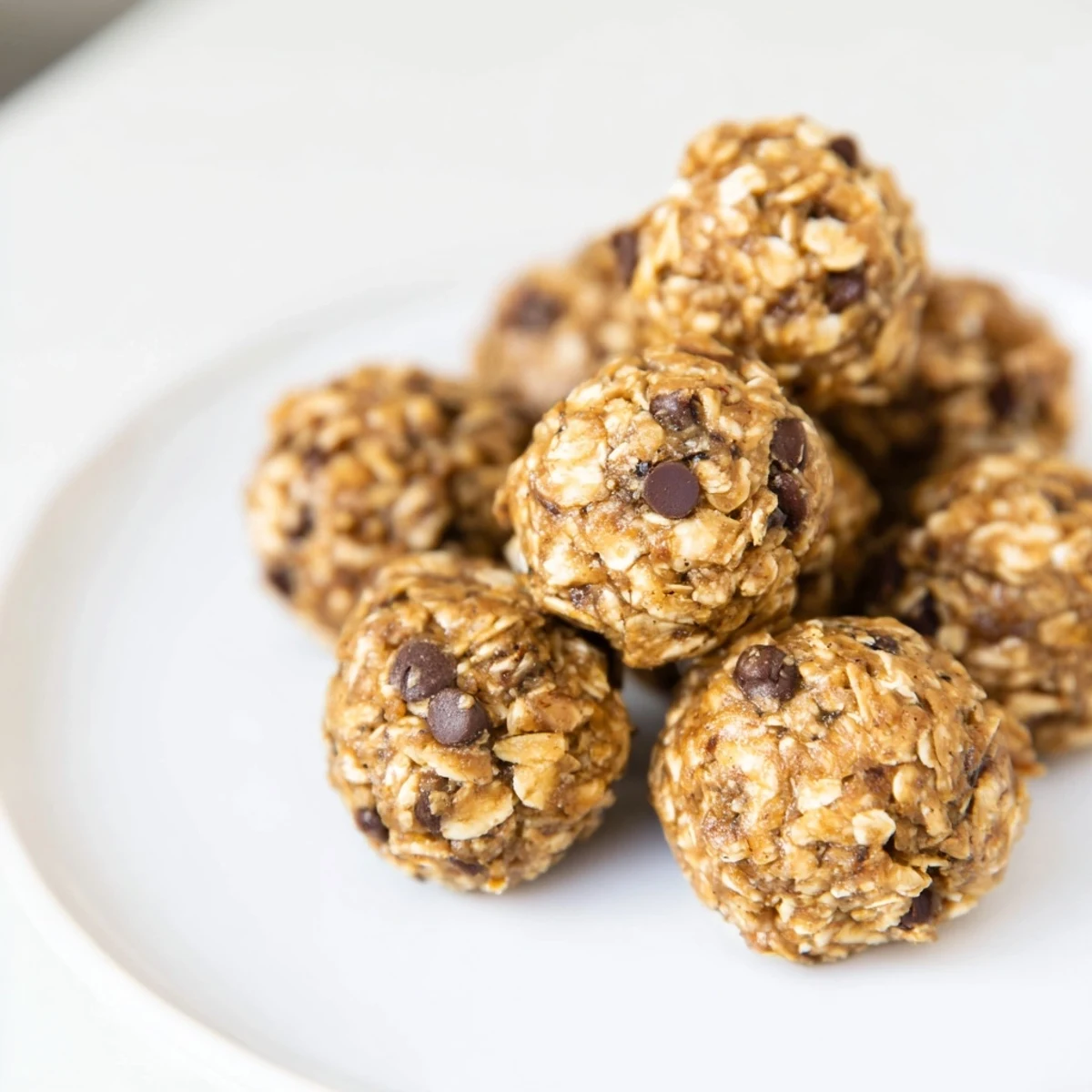 A close-up of Banana Chocolate Chip Energy Balls arranged on a wooden board, showing the texture of oats and mini chocolate chips.  
