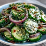 Refreshing Crunchy Cucumber Salad in a white bowl, garnished with fresh dill and sesame seeds, served over ice for a cool crunch. 