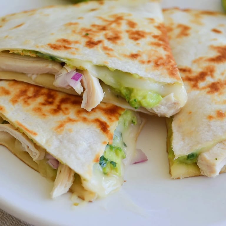 A hand holding a cheesy wedge of Chicken Avocado Quesadilla, highlighting the juicy grilled chicken, red onion, and vibrant green avocado filling.