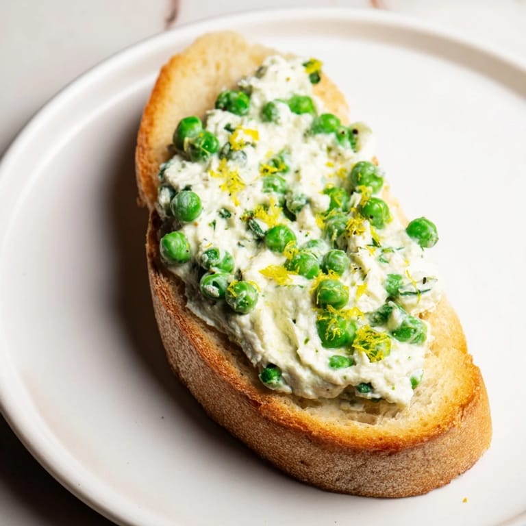 Savory Pea & Mint Ricotta Toast spread thick on crisp sourdough, garnished with mint and lemon, perfect for a light brunch.