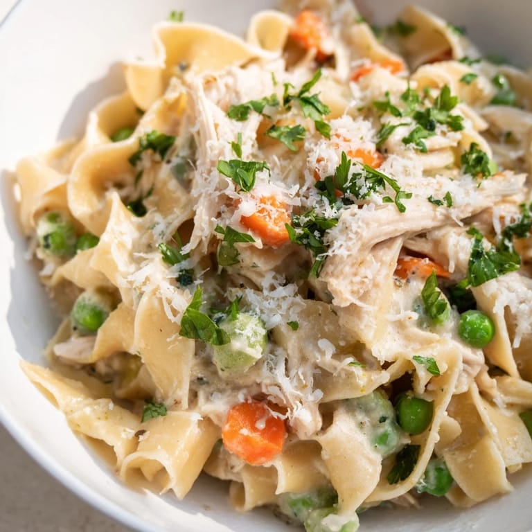 Hearty Spring Chicken Noodle Skillet topped with parsley, paired with crusty bread and lemon wedges on a wooden table.